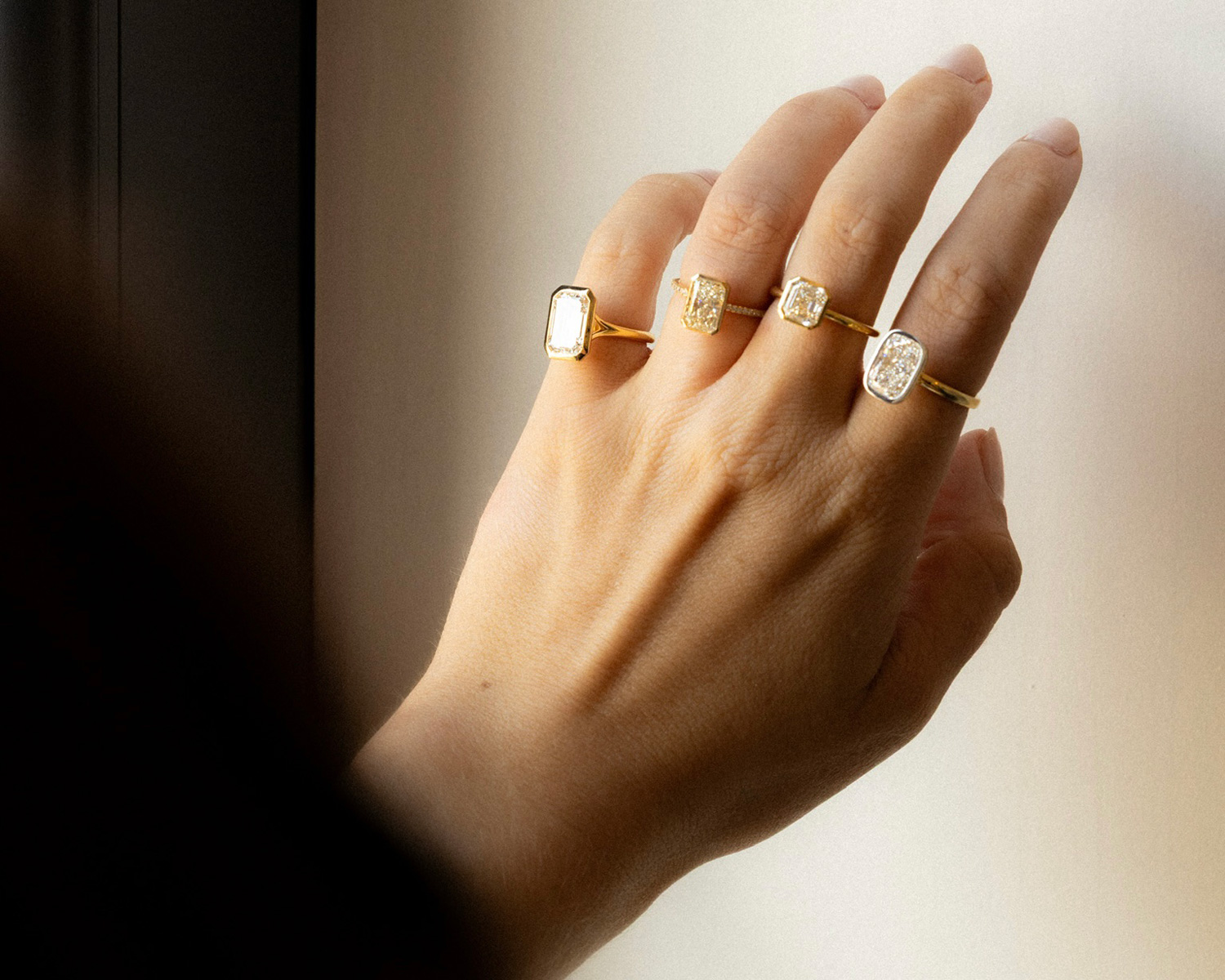An assortment of bezel-set diamond engagement rings featured in on a hand